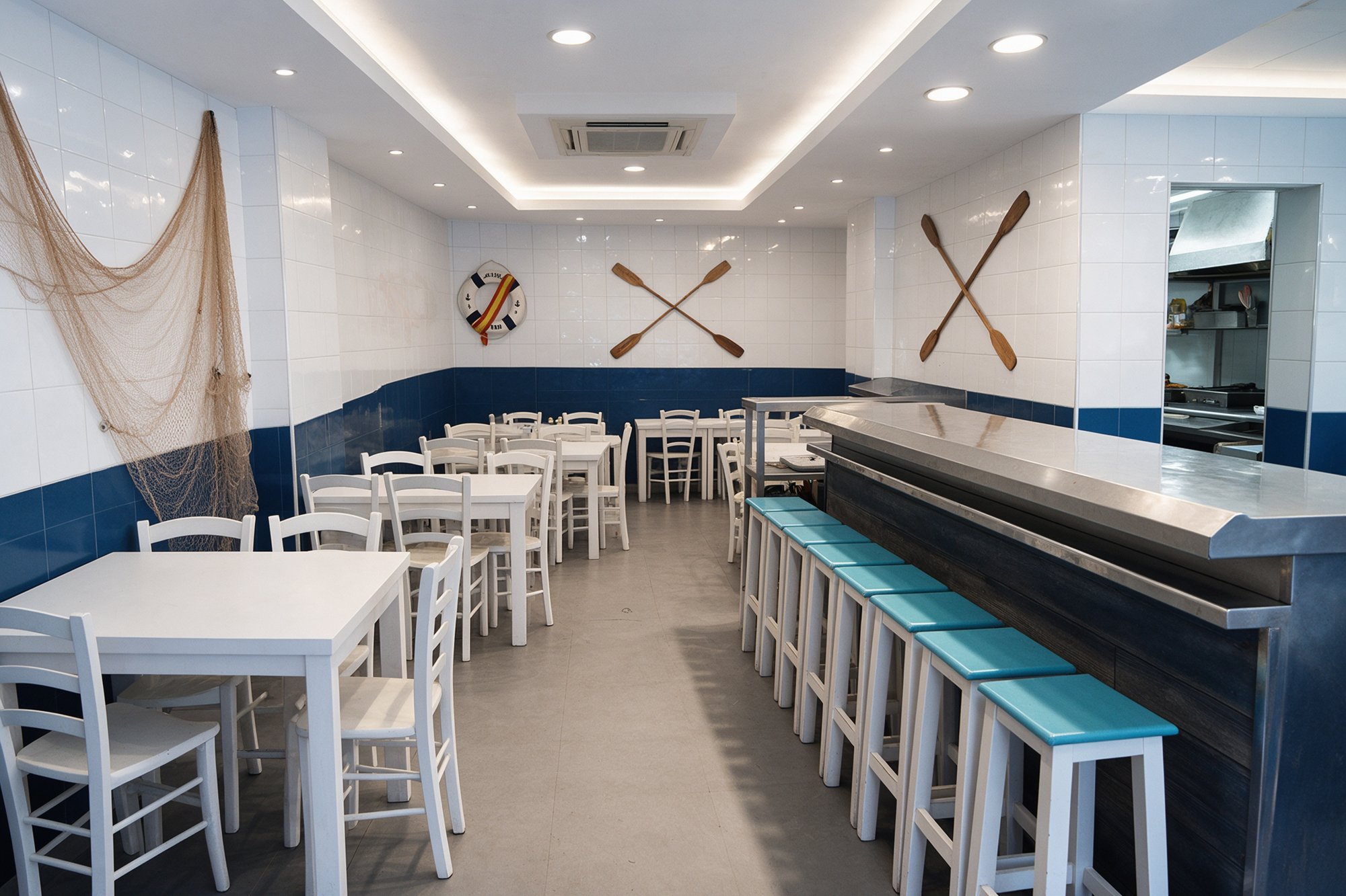 Comedor blanco y azul de freiduría tradicional con taburetes azules, red marinera y remos en la pared